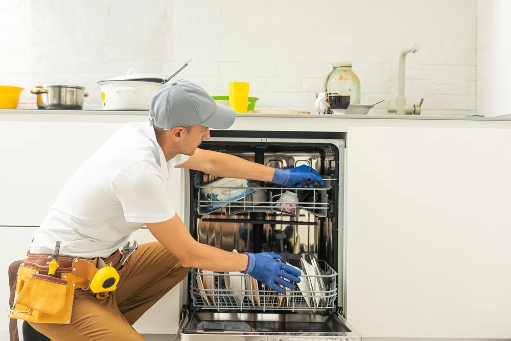 Dishwasher repair technician servicing appliance in Dubai kitchen.